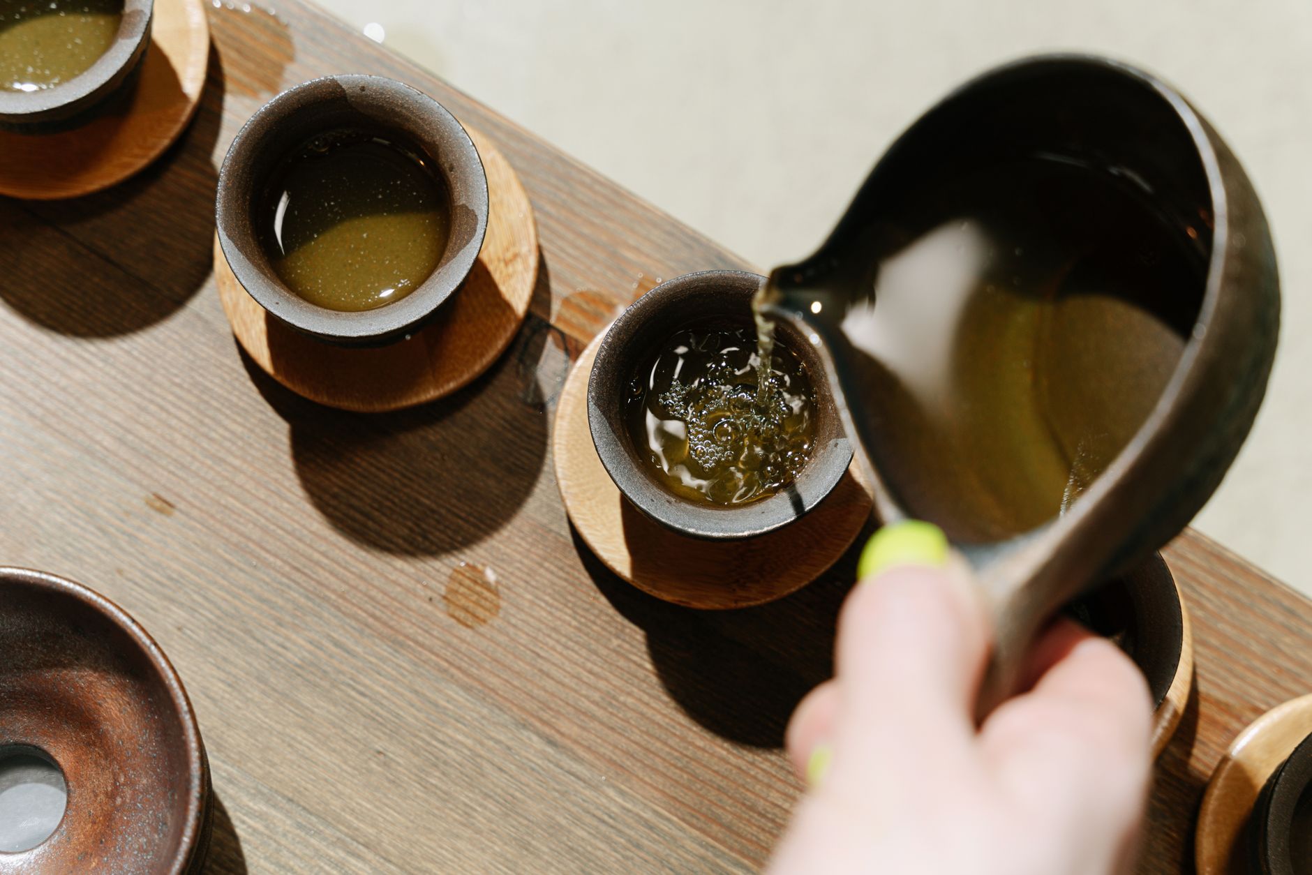 Tea being poured into rustic ceramic cups on a wooden table