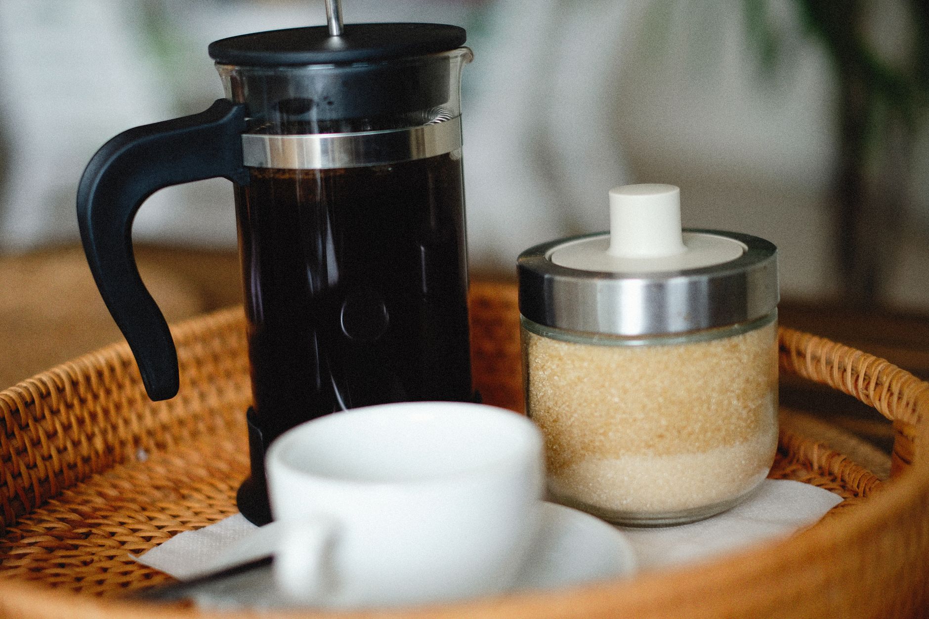 French press, sugar jar, and coffee cup on a wicker tray