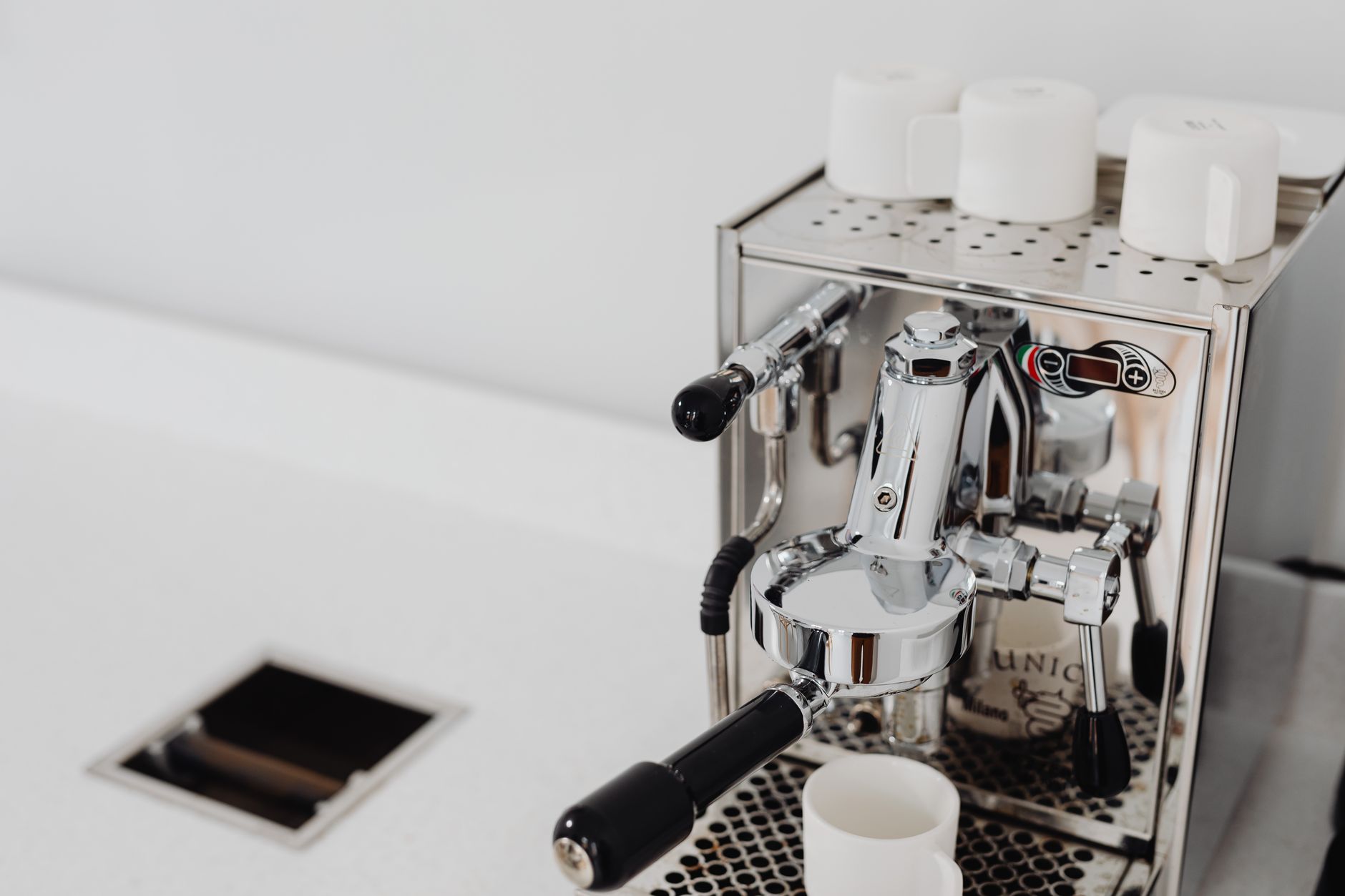 Sleek espresso machine on a white countertop with cups on top